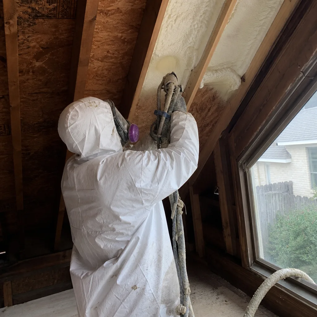 Contractor applying spray foam insulation to attic rafters.